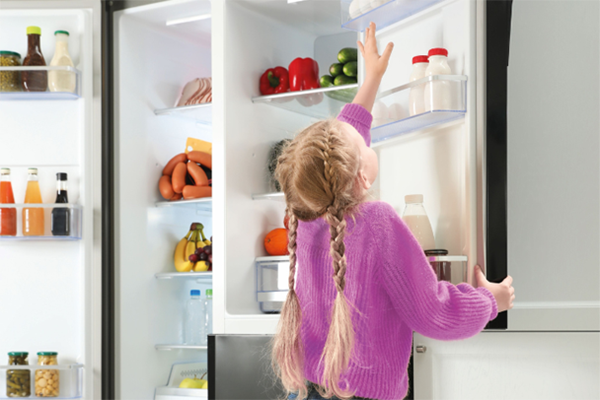Kleines Mädchen, das im modernen Haushaltskühlschrank nach den Eiern greift