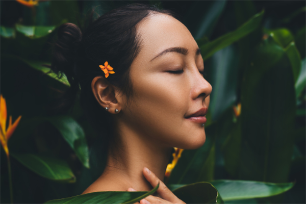 Beautiful young woman with perfect skin and natural make up posing front of plant tropical green leaves background with fern. Teen model with wet hair care of her face and body. SPA, wellness
