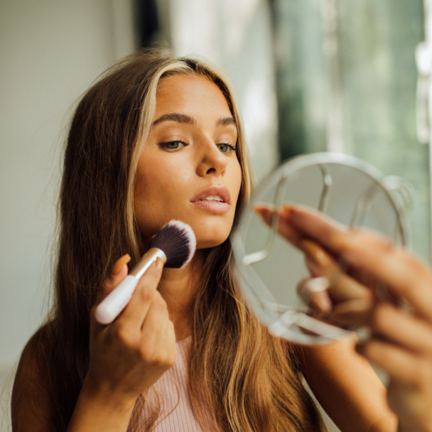 Mujer joven aplicándose maquillaje frente al espejo