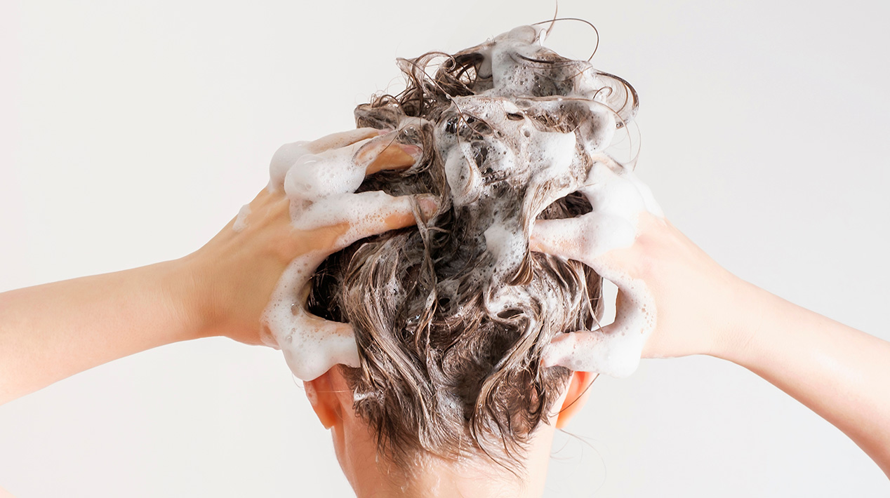 A girl washes her hair with shampoo on a white background, back view.