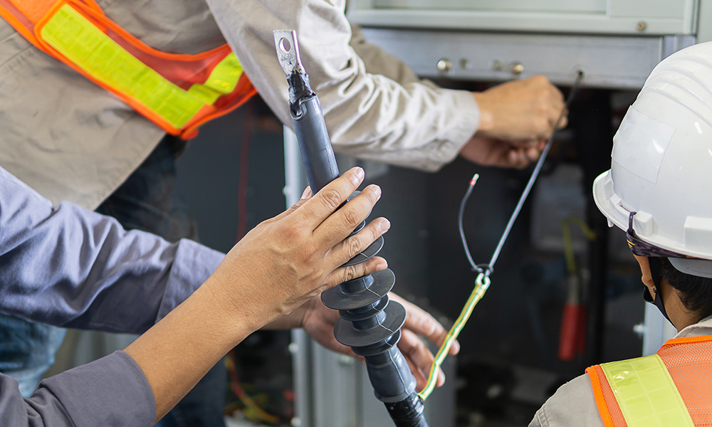 Electrical technicians performing maintenance on industrial control panel, handling insulated tools and wiring for power system safety and reliability.