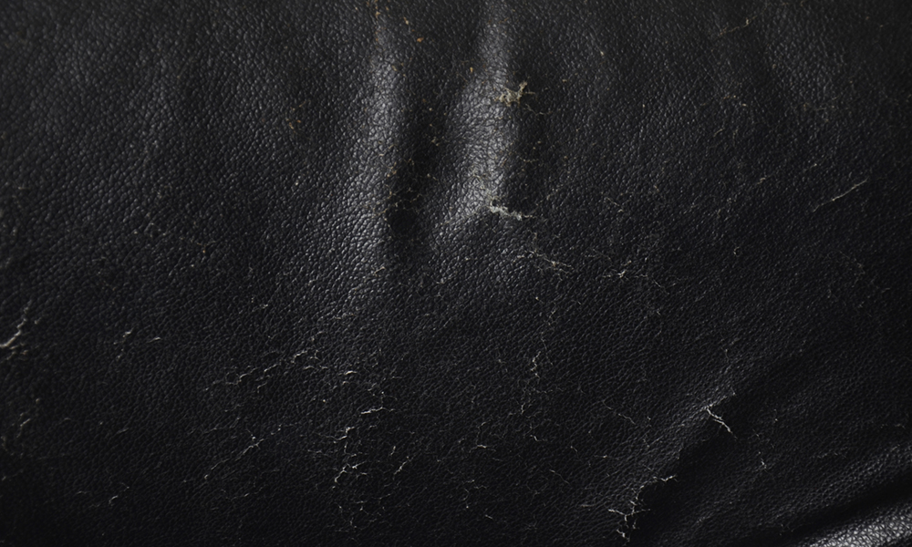 Close-up de uma superfície de couro preto arranhada, mostrando danos que podem ocorrer sem o uso de emulsões de silicone Indusil™ para melhorar a resistência à abrasão e a riscos.