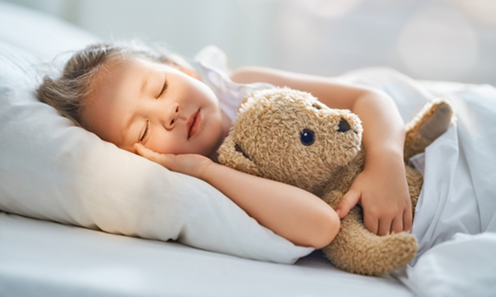 Little girl with teddy bear sleeping on conventional bedding